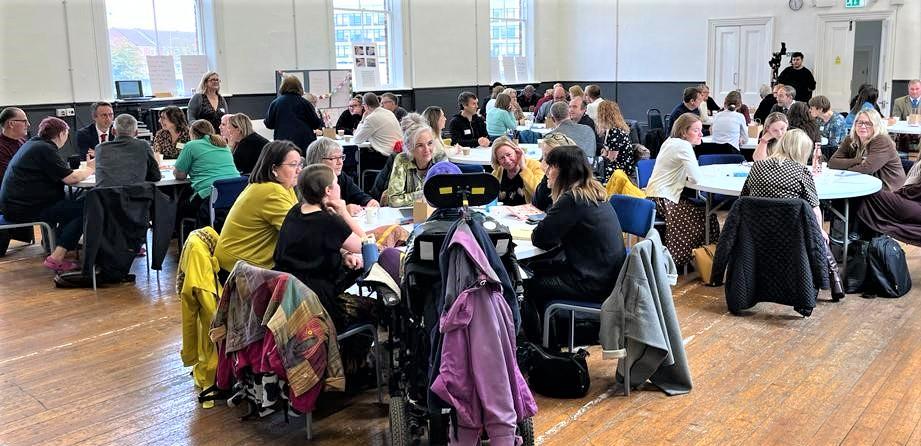 Photograph of people sat round tables in a hall