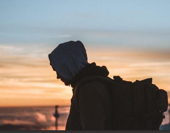 A photogaph of a man with his hud up with a sunset skyline in the background